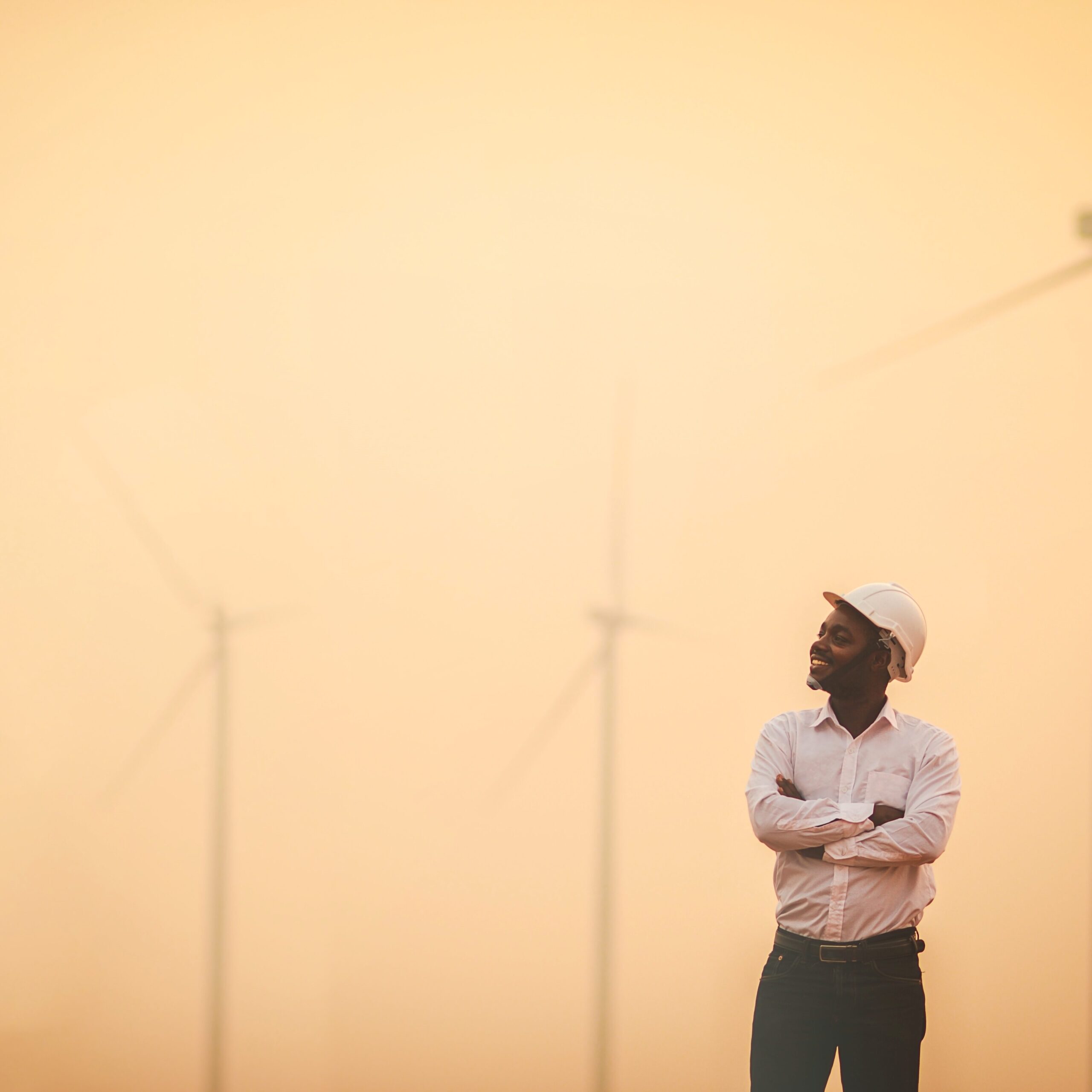 Ein afrikanischer Ingenieur steht mit einem Lächeln vor Windkraftanlagen – Symbol fĂ¼r nachhaltige Energiegewinnung.
